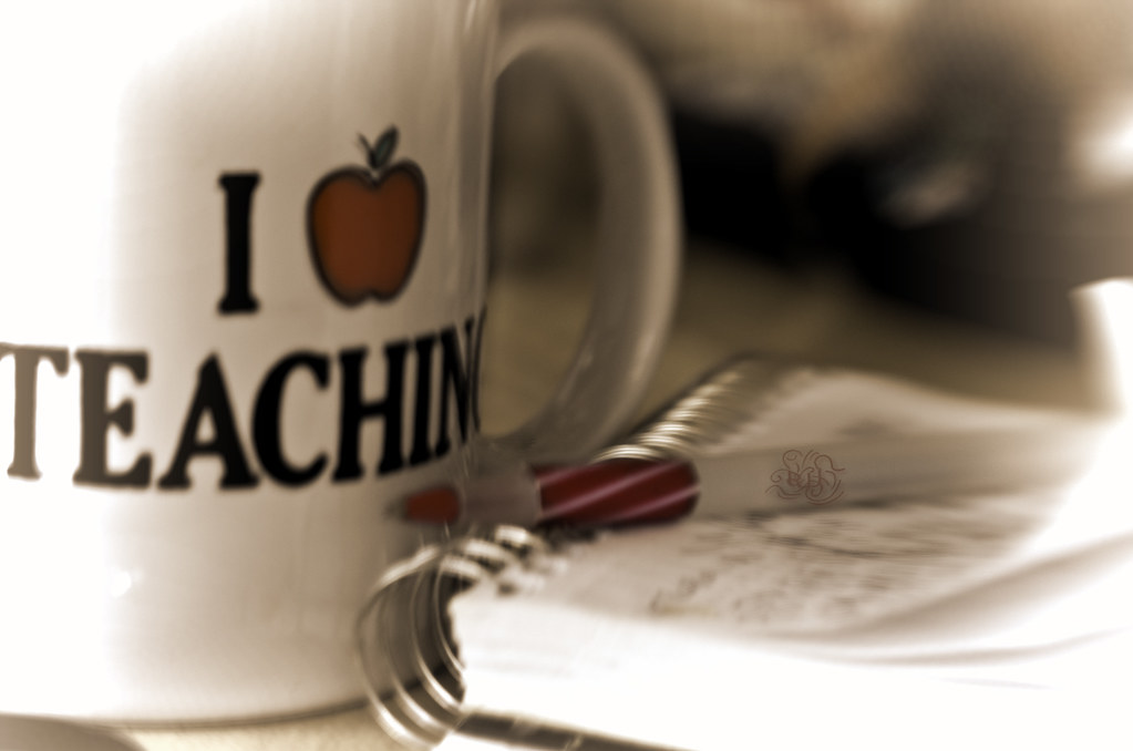 Photo of an "I love teaching" mug, a pen and a notebook.